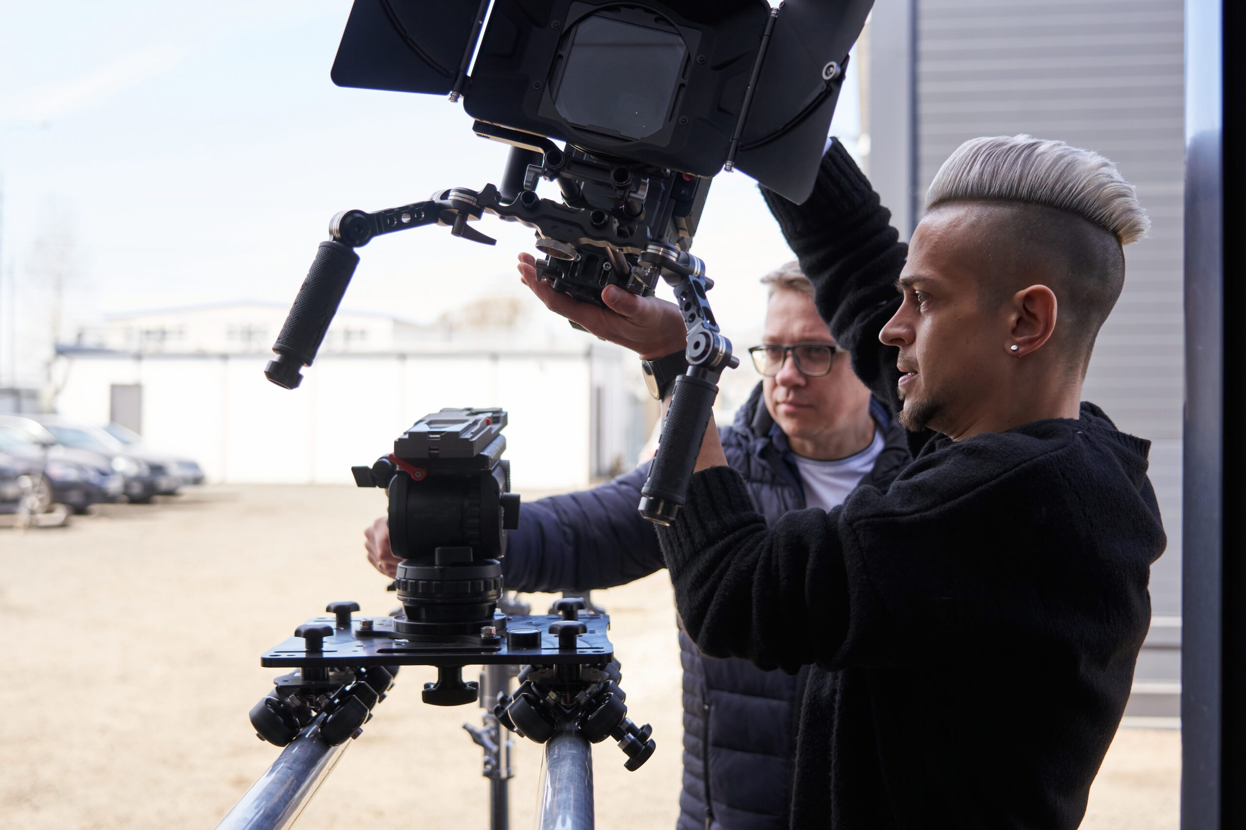 two caucasian men install a large professional camera on a rigging system with wheels on rails. 